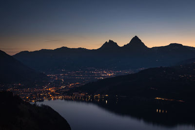 Scenic view of river by silhouette mountains against sky at sunset