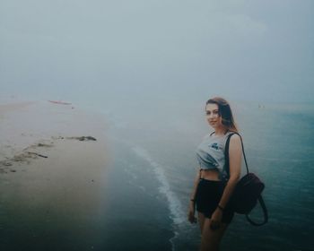 Young woman standing at beach against clear sky