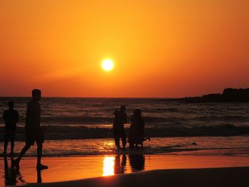 Silhouette people standing on beach against orange sky