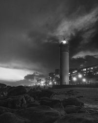 Illuminated lighthouse by buildings against sky at night