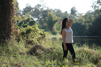 Portrait of young woman standing amidst plants against lake