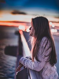 Side view of young woman against sky during sunset
