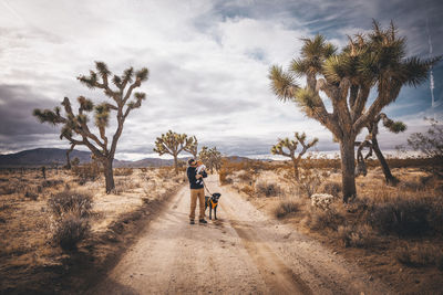 A man with a baby and a dog is standing in a desert of california