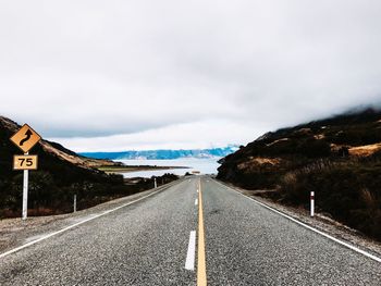 Country road amidst mountains against cloudy sky