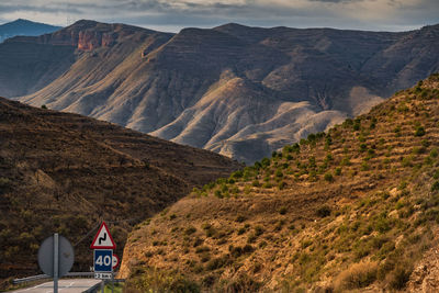 A small road divides terraced hills against  an eroded mountain under darkening winter sky.