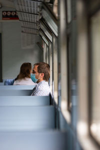 Side view of man wearing mask sitting in train