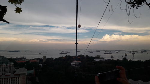 Hand by city against sky during sunset