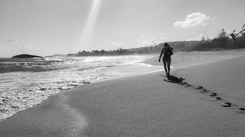 Rear view of man walking on beach against sky