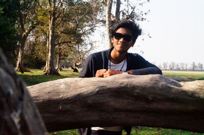 Portrait of young man sitting on grass against trees