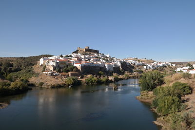Town by river against clear blue sky