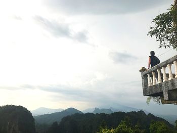 Man sitting on mountain against sky