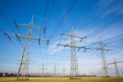 Low angle view of electricity pylons on field against blue sky