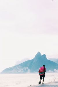 Rear view of man looking at sea against clear sky