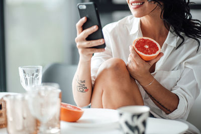 Midsection of woman holding fruit using mobile phone while sitting at home