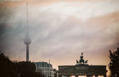 Low angle view of fernsehturm and brandenburg gate against cloudy sky during sunset