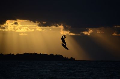 Silhouette of jumping over sea against sky during sunset