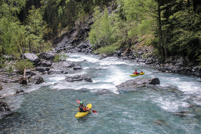 People in river flowing amidst rocks