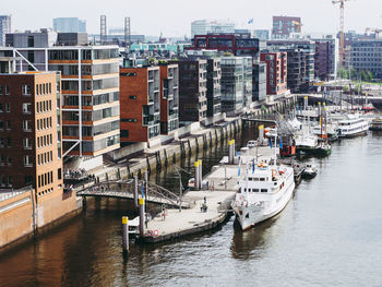 High angle view of boats moored at harbor by buildings in city against sky