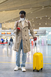 Black traveler man with wear face mask during covid-19 pandemic standing at airport terminal. 