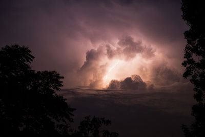 Low angle view of storm clouds over silhouette trees