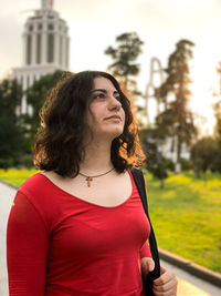 Young woman looking away standing against sky at sunset