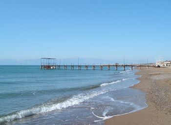 Pier at beach against clear blue sky on sunny day