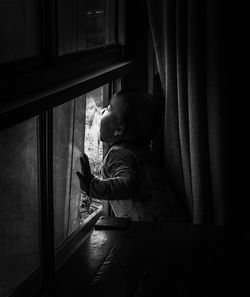 Side view of baby boy looking through window at home