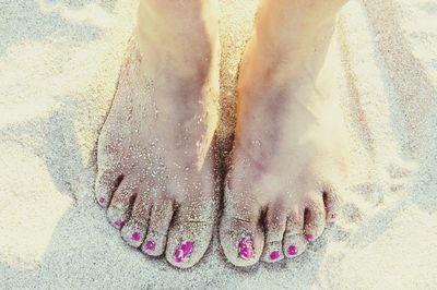 Low section of woman with pink nail polish standing on sandy beach