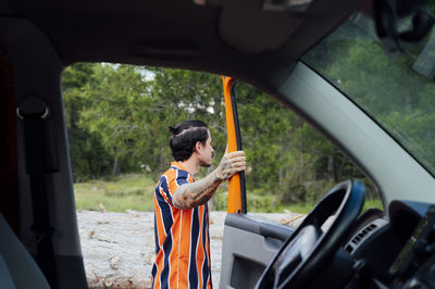 Side view of male traveler standing near opened door of van parked in woods in summer