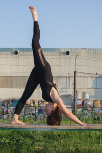 Woman doing yoga on bench against sky