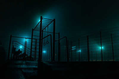 Low angle view of illuminated lights by fence against sky at night