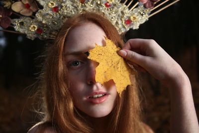 Close-up portrait of young woman holding maple leaf