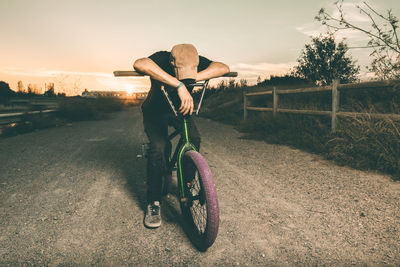 Man sitting on bicycle against sky during sunset