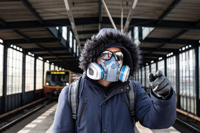Portrait of young man standing at railroad station with mask on