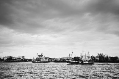 Boats sailing in sea against cloudy sky