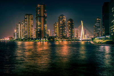 Illuminated city by river against sky at night