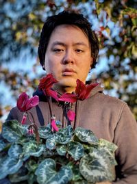Portrait of young asian man with red flowering cyclamen plant against trees.