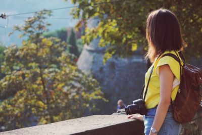 Side view of woman with camera looking at view against trees