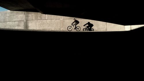 Side view of man riding bicycle below bridge on sunny day