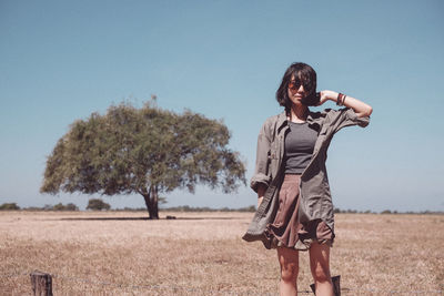 Portrait of young woman standing on field against blue sky