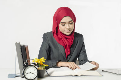 Young woman sitting on table against white background