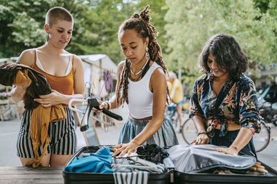 Female partners packing dress in suitcase on table at flea market