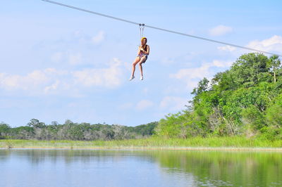 Low angle view of woman hanging from zip line over lake against sky