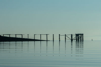 Reflection of pier in sea against clear sky