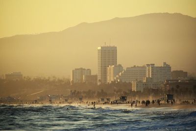 Sea by cityscape against clear sky during sunset