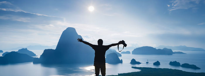 Rear view of man with arms raised standing on mountain against sky