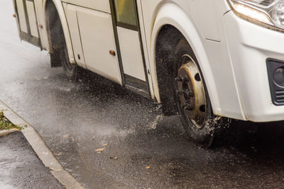 White municipal bus moving on rainy road with water splashes