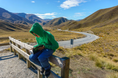 Boy sitting on fence against sky