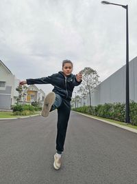 Portrait of teenage girl with umbrella on road against sky