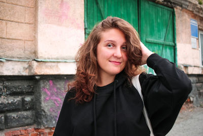 Smiling young woman in black hoodie against building background